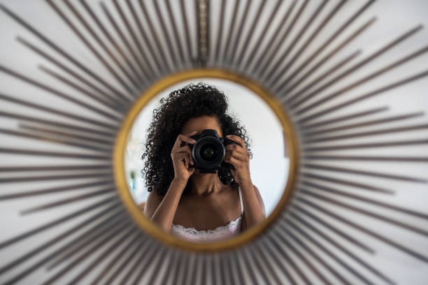 Black woman holding a professional camera taking a picture of her reflection on the mirror