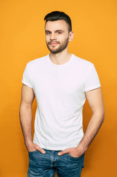 istock Stature and well-built man in denim jeans and white basic T-shirt with a beard and smooth dark hair is standing in front of orange background. 1143523052