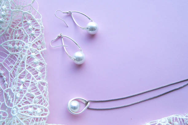 bellissimi gioielli in argento lucido perla, orecchini glamour alla moda, catena su sfondo viola rosa con pizzo squisito. lay piatto, vista dall'alto - pearl necklace earring jewelry foto e immagini stock