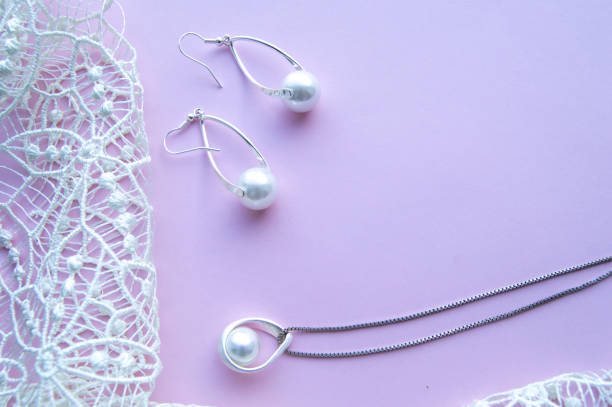 美しいシルバー光沢のある真珠の宝石類、トレンディなグラマラスイヤリング、ピンクの紫色の背景に絶妙のレースでチェーン。フラットレイ, トップビュー - pearl necklace earring jewelry ストックフォトと画像