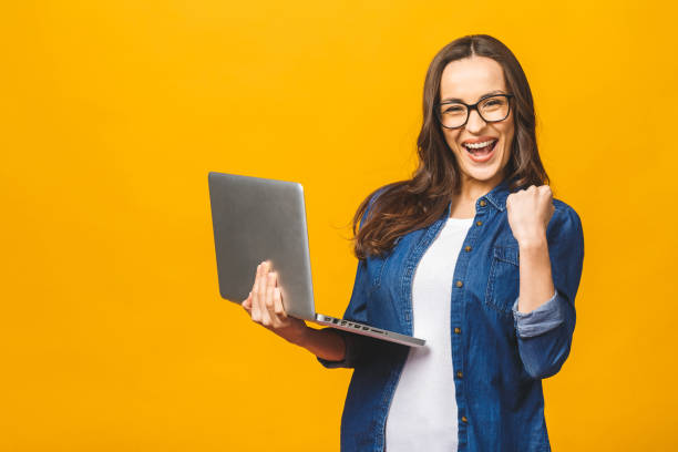 Successful woman with a laptop computer and arms up - isolated over yellow Successful woman with a laptop computer and arms up - isolated over yellow excitement laptop stock pictures, royalty-free photos & images