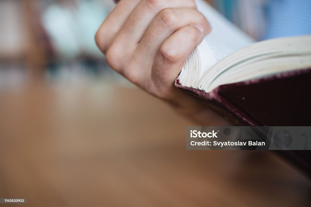 Male hand holds the opened book. View of the book back close-up. Arm Stock Photo