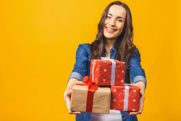 istock Young smiling model hold gift box. Woman isolated on yellow background. 1143535341