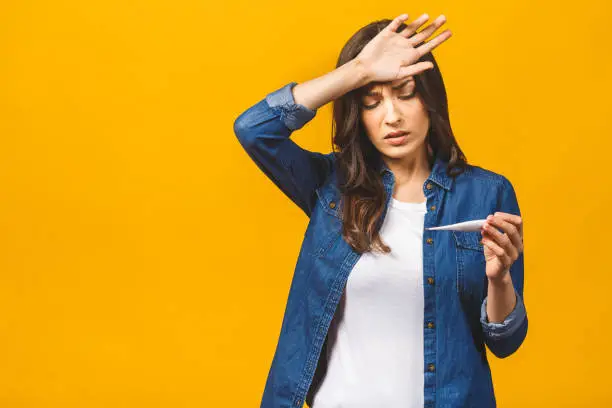 Young woman having flue taking thermometer. Isolated against yellow background. Beautiful young woman is sick with a high temperature, a thermometer, isolated close-up. Cold, flu concept.