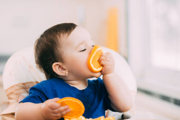 A Little Girl In A Blue Tshirt And A Blue Plate Sitting In A Childs Chair  Eating An Orange Stock Photo - Download Image Now - iStock