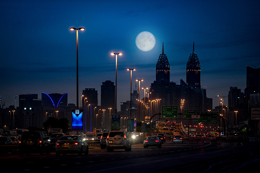 Street with skyline Dubai arab view of crossroad with cars palace background, remembering of buildings on night illuminated by full moon United Arabian Emirates watching tall tower middle-east Asia