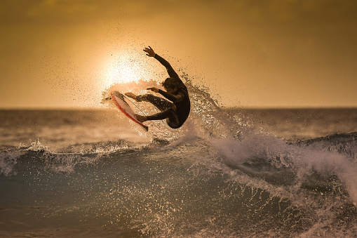 Surfista saltando en la ola en la hora dorada en una playa tropical deportivo joven hombre haciendo trucos sobre las olas con un tablero SUF Extreme deporte y acción en el agua en el atardecer con espuma y spray photo
