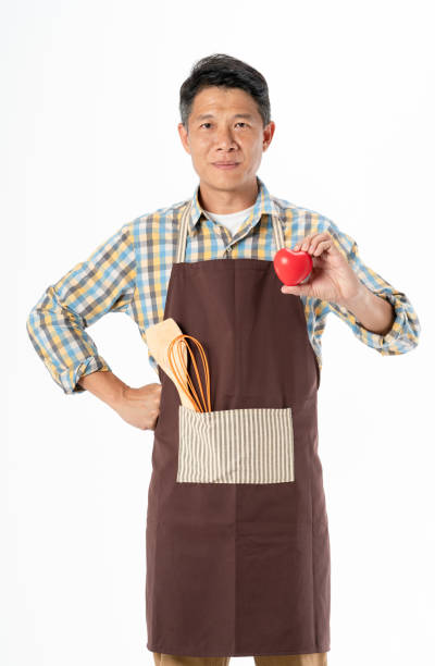 Asia man in apron with kitchen equipment holding red heart shape on white background