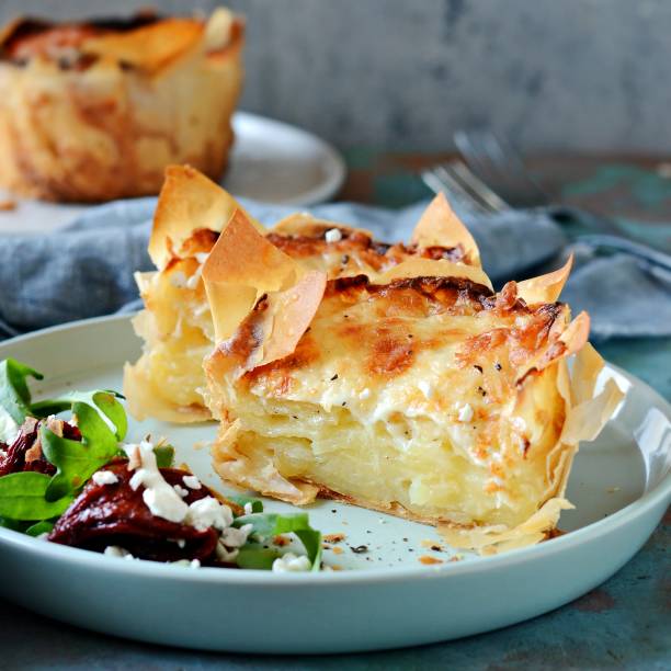 kartoffelgratin in filo-teig gebacken, mit knuspriger käsekruste und mit einem salat aus rucola, sonnengetrockneten tomaten und käse - dauphinois stock-fotos und bilder