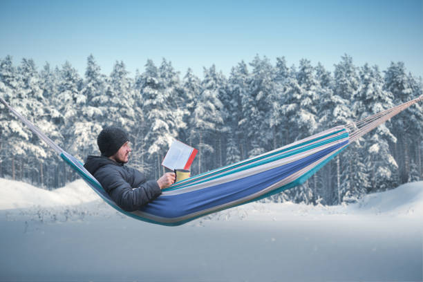 mężczyzna czyta czerwoną książkę w hamaku w zimowym lesie. kubek z gorącym napojem w ręku - scandinavian peninsula winter pine tree tree zdjęcia i obrazy z banku zdjęć