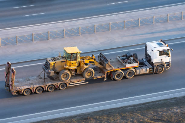 istock Truck with a long trailer platform for transporting heavy machinery, loaded tractor with a bucket. Highway transportation. 1143551644