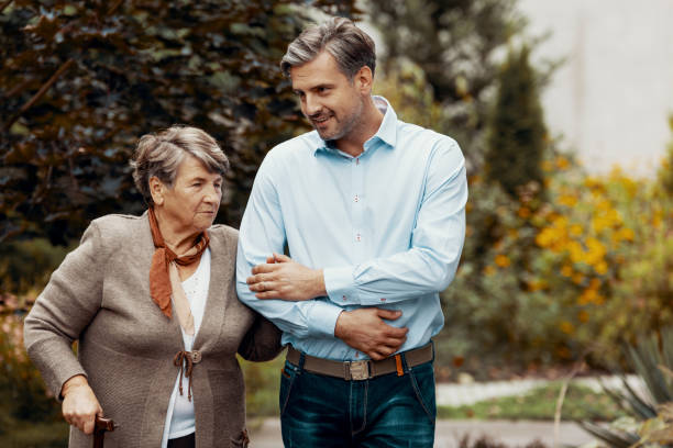 istock Smiling man supporting senior woman while walking in the garden 1143559012