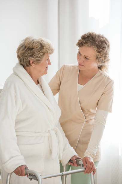 istock Senior woman in a bathrobe with a walker supported by a nurse 1143561075