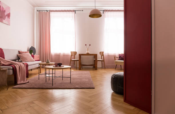 istock Wooden table on pink carpet in flat interior with blanket on sofa and drapes at window. Real photo 1143563626