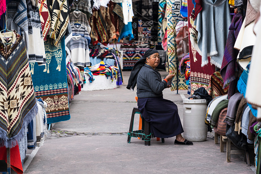 Otavalo, Ecuador - February 23, 2019: Older Indian woman sells products of weaving on local market.