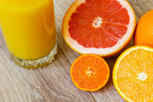 still life - various whole and cut citrus fruits and glass of orange juice on a wooden table