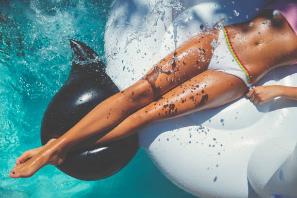 femme flottant sur un gonflable blanc dans la piscine dans un bikini blanc. - bikini human leg sensuality women photos et images de collection