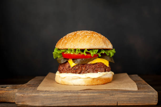 istock Homemade hamburger with lettuce, tomato, cheese and cucumber on a cutting board 1143589433