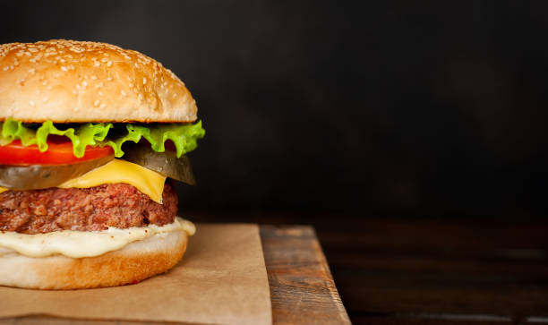 istock Homemade hamburger with lettuce, tomato, cheese and cucumber on a cutting board 1143589455