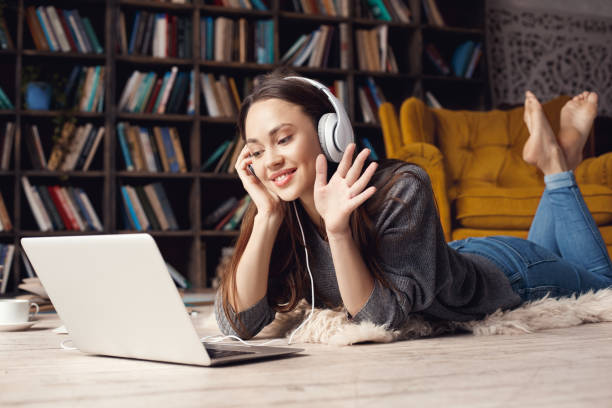 jeune étudiant de femme dans la bibliothèque à la maison se trouvant l’appel vidéo - armchair comfortable relaxation headphones photos et images de collection