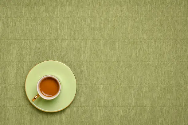 green cup of coffee against green Italian crepe paper background with a copy space