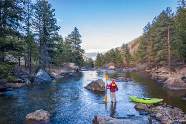 male paddler with an inflatable whitewater kayak - Poudre River below Mishiwaka, Colorado in early spring
