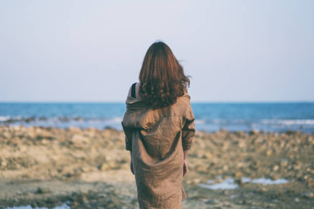 istock woman walking on the beach by the seashore 1143628854