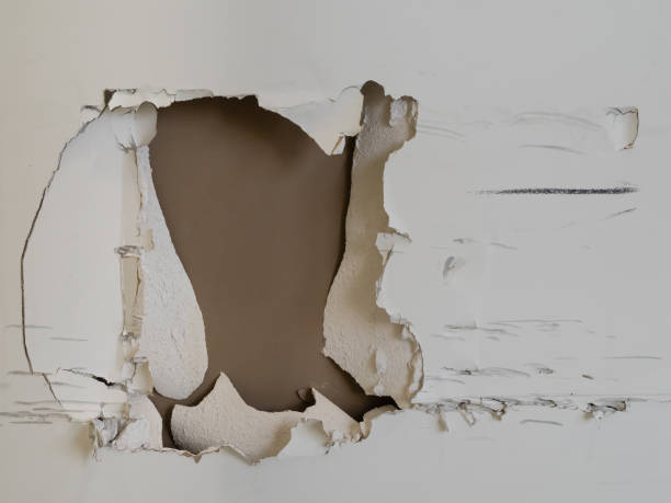 Large hole with skid marks and cracks in drywall of a cream wall Very large hole caused by impact in the side of a cream wall showing brown underneath with cracks, skid marks and damage painted drywall texture stock pictures, royalty-free photos & images