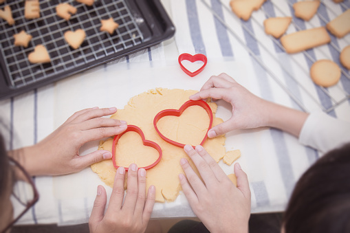 Close up hands of little asian girl and her mother baking cutter cookies heart shape in the kitchen. Happy asian family and motherâs day valentineâs day concept. background and banner