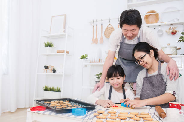 小さなアジアの女の子と彼女の両親が台所でケーキやクッキーを焼くの肖像画。ハッピーアジアの家族と motherâs の日のコンセプト - bread bakery women cake ストックフォトと画像