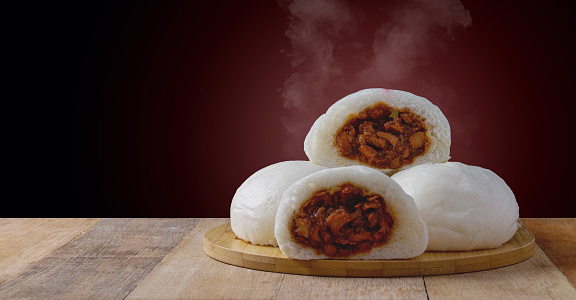 Steamed buns with red pork filling on a wooden tray and placed on a wooden table and a black red background