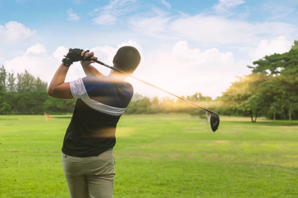 Close up Golfer is driving golf ball to green course with light flare. stock photo