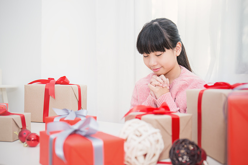 Portrait of little cute asian girl praying by pie of gift box, Asian teenage girl making a wish for christmas concept