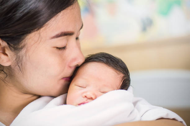 portrait of beautiful young asian mother kissing  her newborn baby, copy space with bed in the hospital background. - mother baby new kissing imagens e fotografias de stock