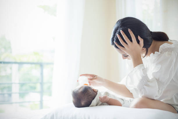 asiatique mère pépinière alimentation bouteille de lait de formule pour bébé nouveau-né dans le lit souffrant de dépression post-natale. soins de santé mère monoparentale concept stressant. - domestic life sadness family bed photos et images de collection