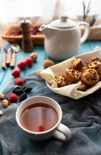 A cup of tea with homemade cookies and a white teapot on a wooden table against the background of a window with sunny morning light and shadow. Early breakfast concept. Free space for text.