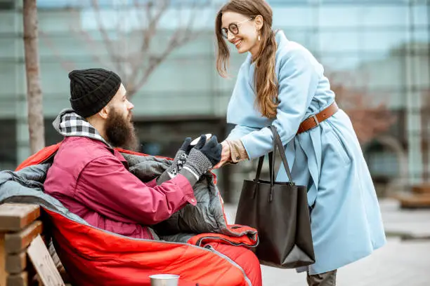 Photo of Woman giving a drink to a homeless beggar