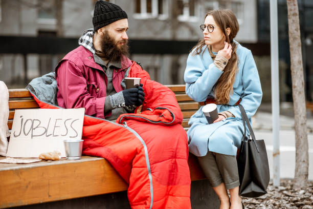 Homeless beggar with young woman listening to his story Homeless beggar with young woman listening to his sad story while sitting together on the bench outdoors. Concept of a human understanding begging currency beggar poverty stock pictures, royalty-free photos & images