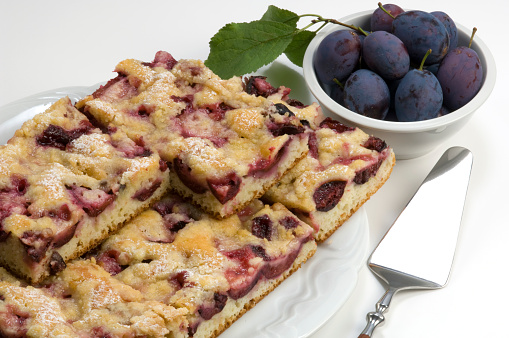 Plum Pie on white plate and plums with leaves.