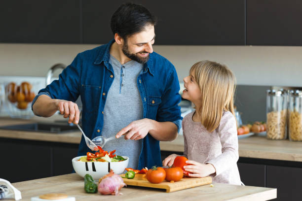 jeune homme attirant avec sa petite fille mignonne faisant la salade ensemble sur la cuisine à la maison - tomato small food vegetable photos et images de collection