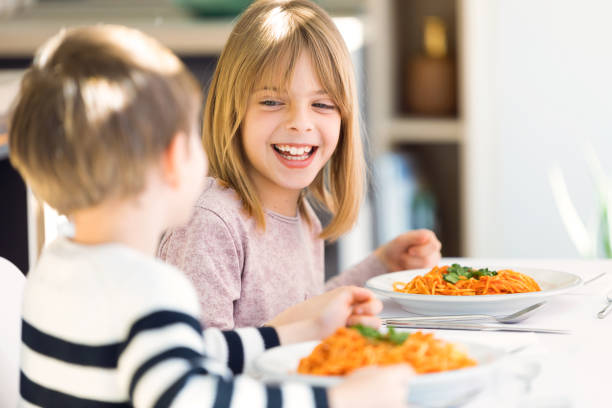 enfants de sourire ayant l’amusement tout en mangeant des spaghettis avec la sauce tomate dans la cuisine à la maison. - healthy lifestyle people eating sister photos et images de collection