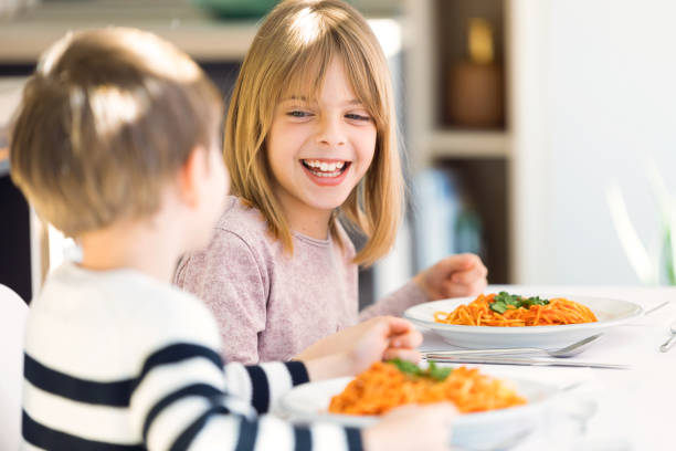 uśmiechnięte dzieci bawiące się podczas jedzenia spaghetti z sosem pomidorowym w kuchni w domu. - spaghetti sauces pasta vegetable zdjęcia i obrazy z banku zdjęć