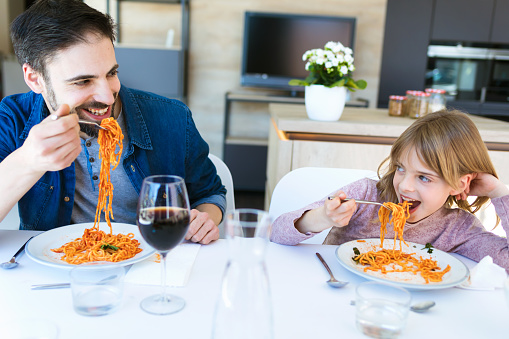 Shot of handsome young father and her beautiful having fun while eating pasta with tomato sauce for lunch in the kitchen at home.