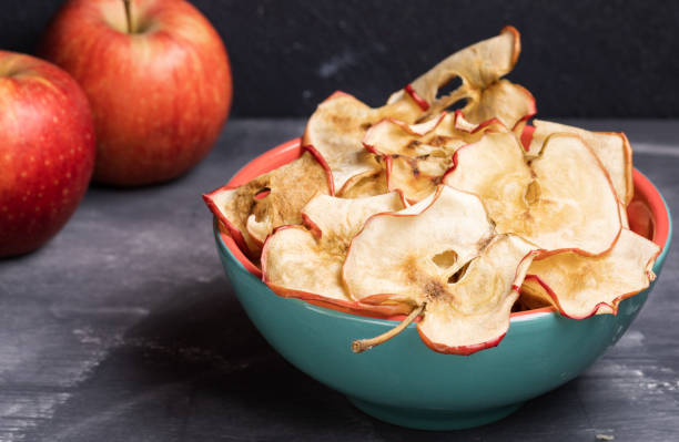 istock Close-up healthy  apple chips in turquoise ceramic bowl and two whole apples on dark grey background. 1143692029