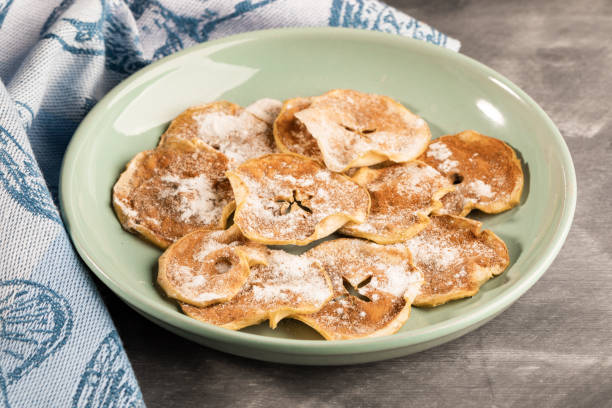 istock Close-up apple chips sprinkled with powdered sugar and cinnamon on plate and  towel on grey background. 1143692031