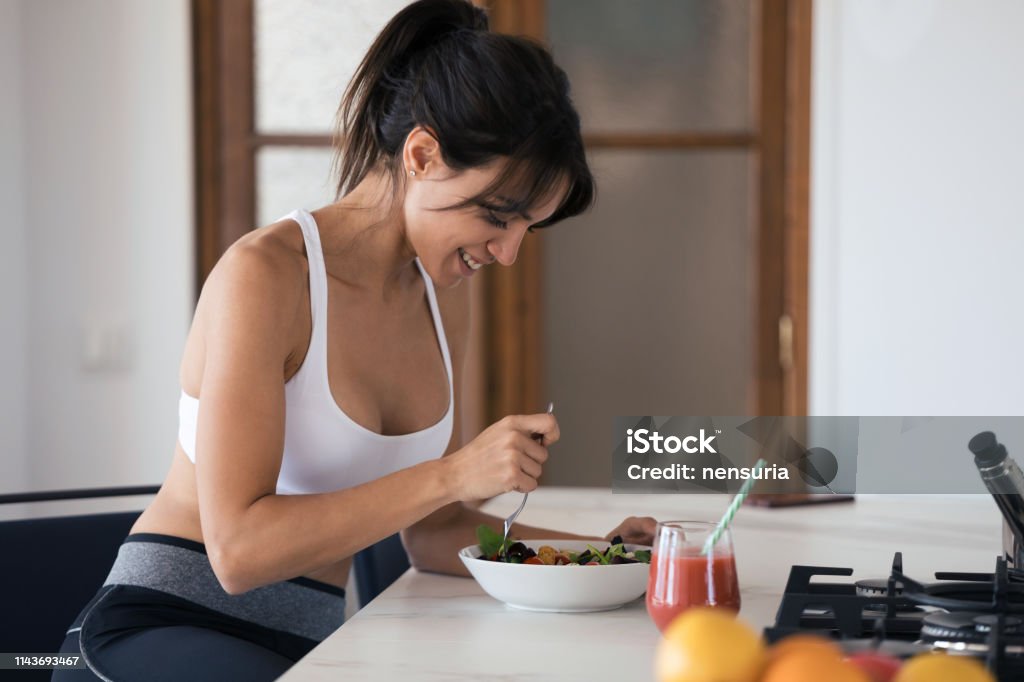 Sportliche junge Frau isst Salat und trinkt Fruchtsaft in der Küche zu Hause. - Lizenzfrei Essen - Mund benutzen Stock-Foto