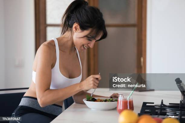 Sportliche Junge Frau Isst Salat Und Trinkt Fruchtsaft In Der Küche Zu Hause Stockfoto und mehr Bilder von Essen - Mund benutzen