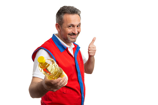 Smiling supermarket or hypermarket male employee making thumb up like gesture to sunflower oil bottle as advertising store concept isolated on white background