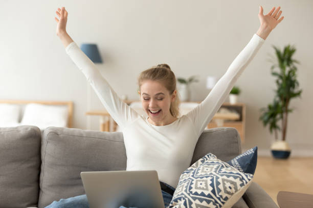 Excited smiling woman celebrating online win, using laptop at home