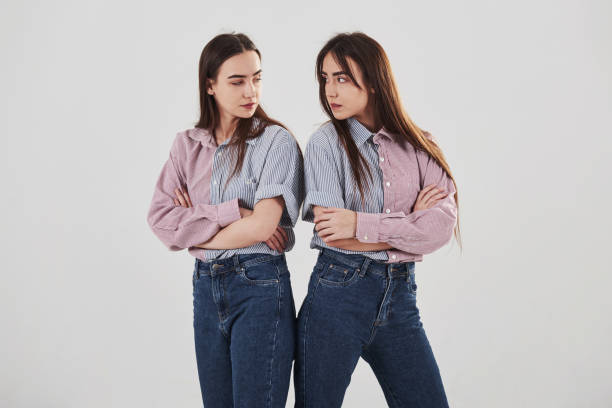 offensé et regarder les autres avec la colère. deux sœurs jumelles debout et posant dans le studio avec le fond blanc - seeing double photos et images de collection